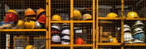 Multiple yellow, white, and orange construction helmets are stored on shelves behind a yellow metal grid, likely for workers’ use at a construction site.